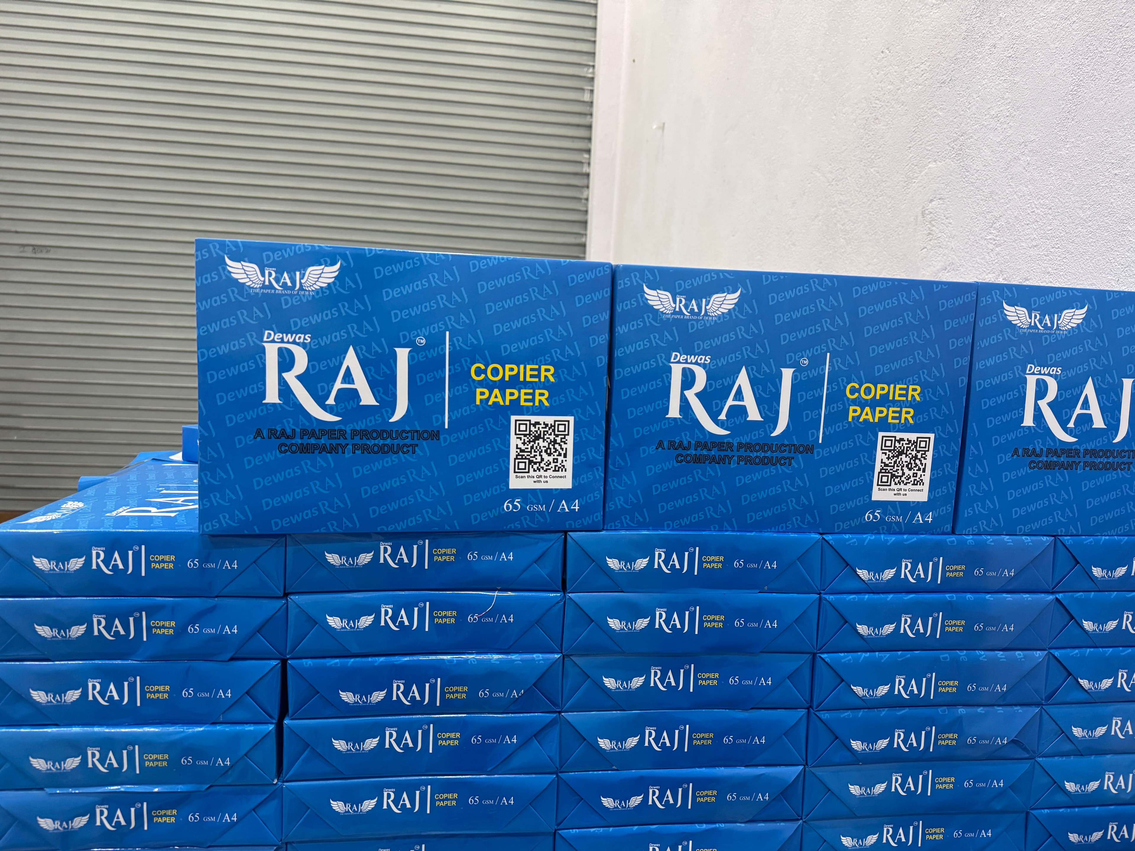 Close-up of Dewas Raj 65 GSM A4 copier paper cartons with brand logo and QR code
